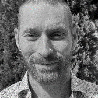 A man with a beard and mustache in front of bushes.